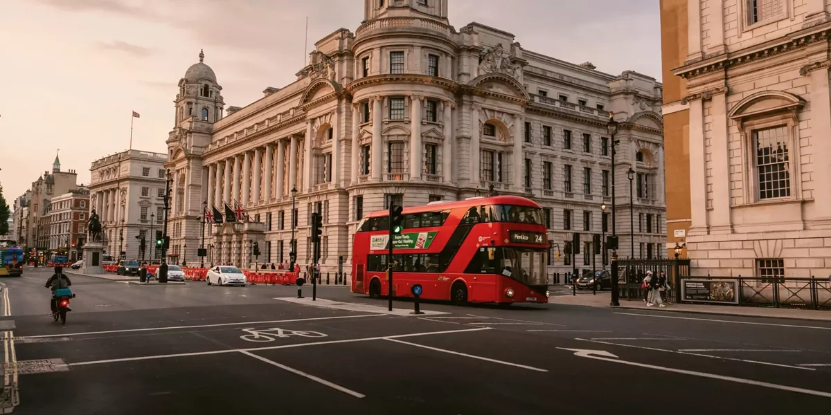 A classic red double-decker bus travels through central London at sunset on the Contiki London Mini Break