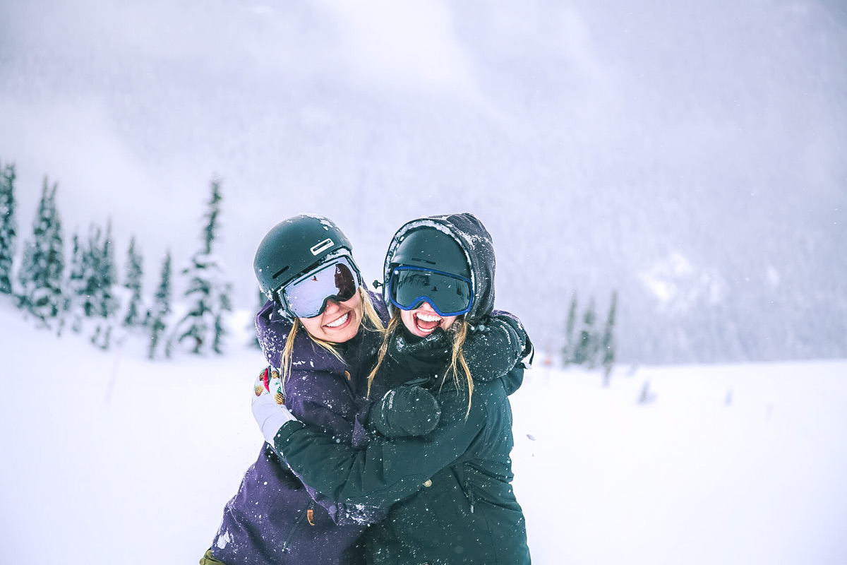 Friends Laughing And Hugging Each Other Wearing Ski Equipment
