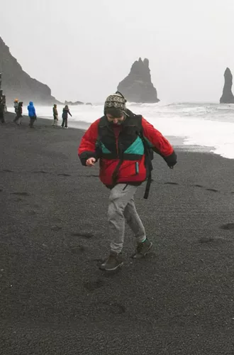 Traveller walks along Reynisfjara Black Sand Beach with the Reynisdrangar sea stacks in Iceland on the Contiki Best of Iceland Tour