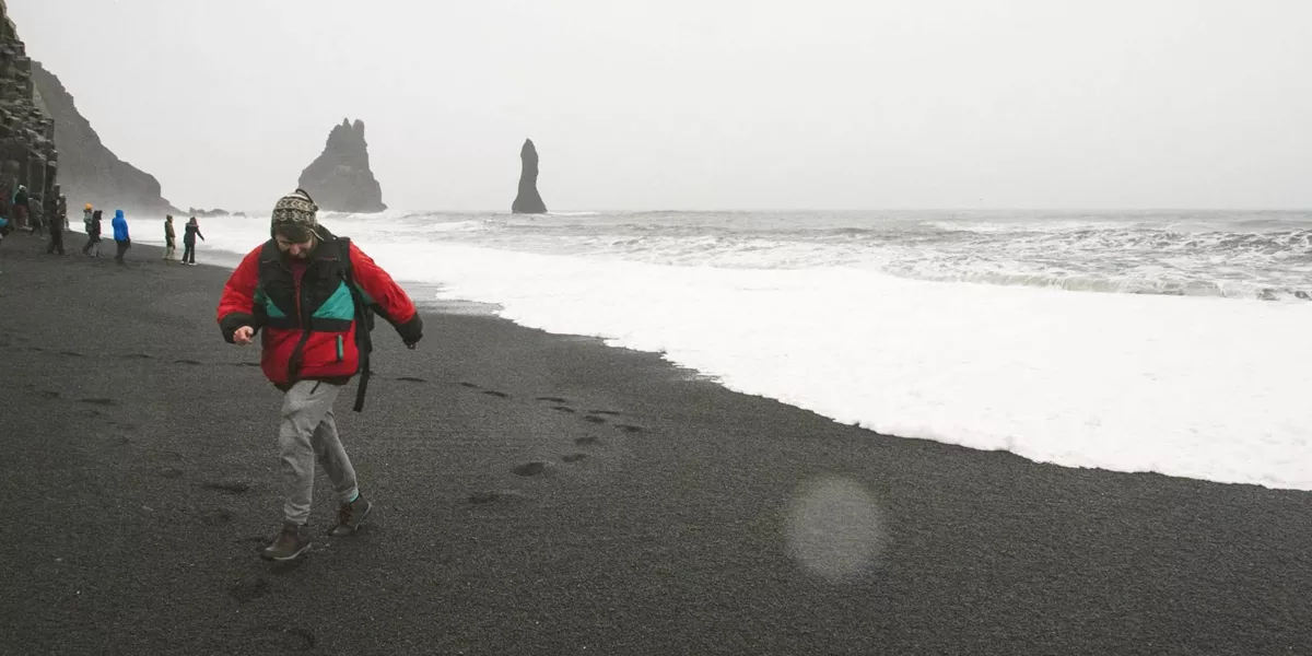 Traveller walks along Reynisfjara Black Sand Beach with the Reynisdrangar sea stacks in Iceland on the Contiki Best of Iceland Tour