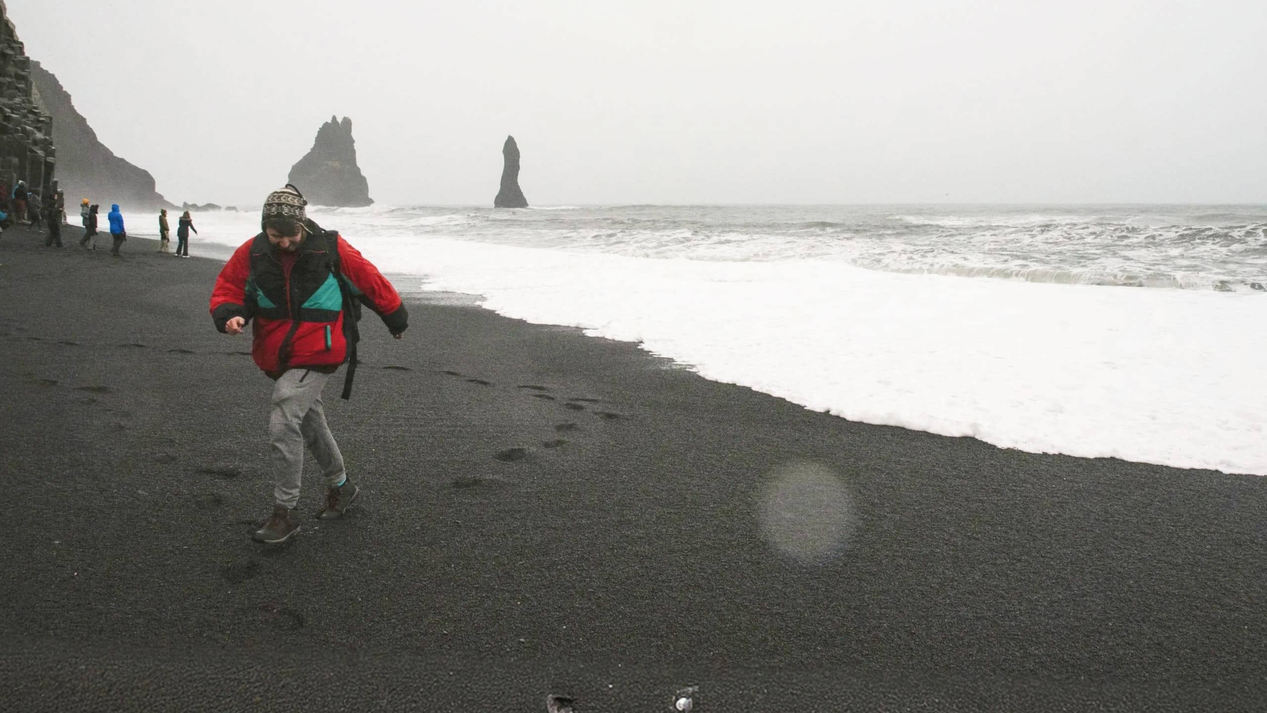 Traveller walks along Reynisfjara Black Sand Beach with the Reynisdrangar sea stacks in Iceland on the Contiki Best of Iceland Tour
