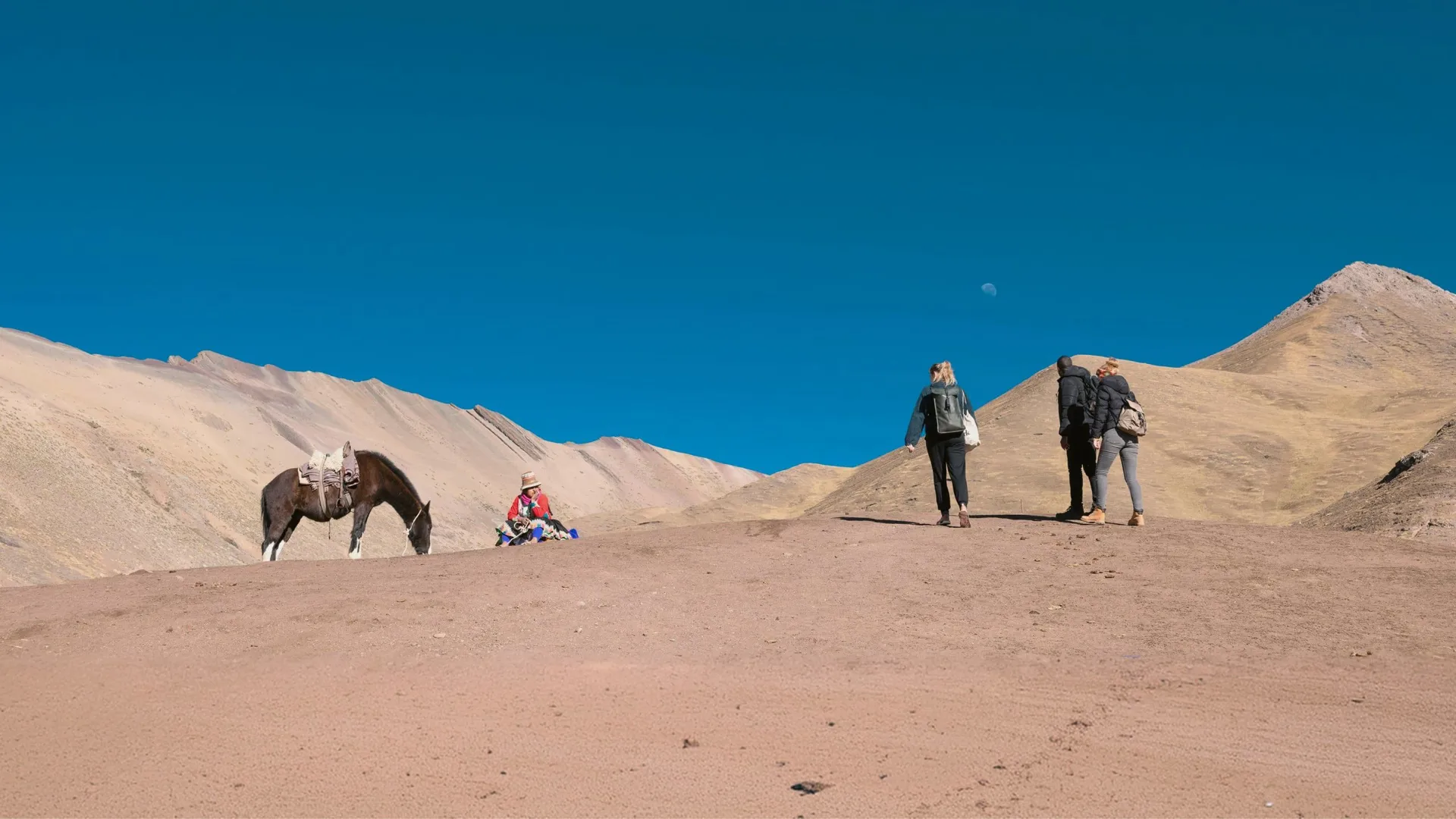 Travellers walking through the Peruvian Andes, with a local person and saddled horse against a dramatic mountain landscape.