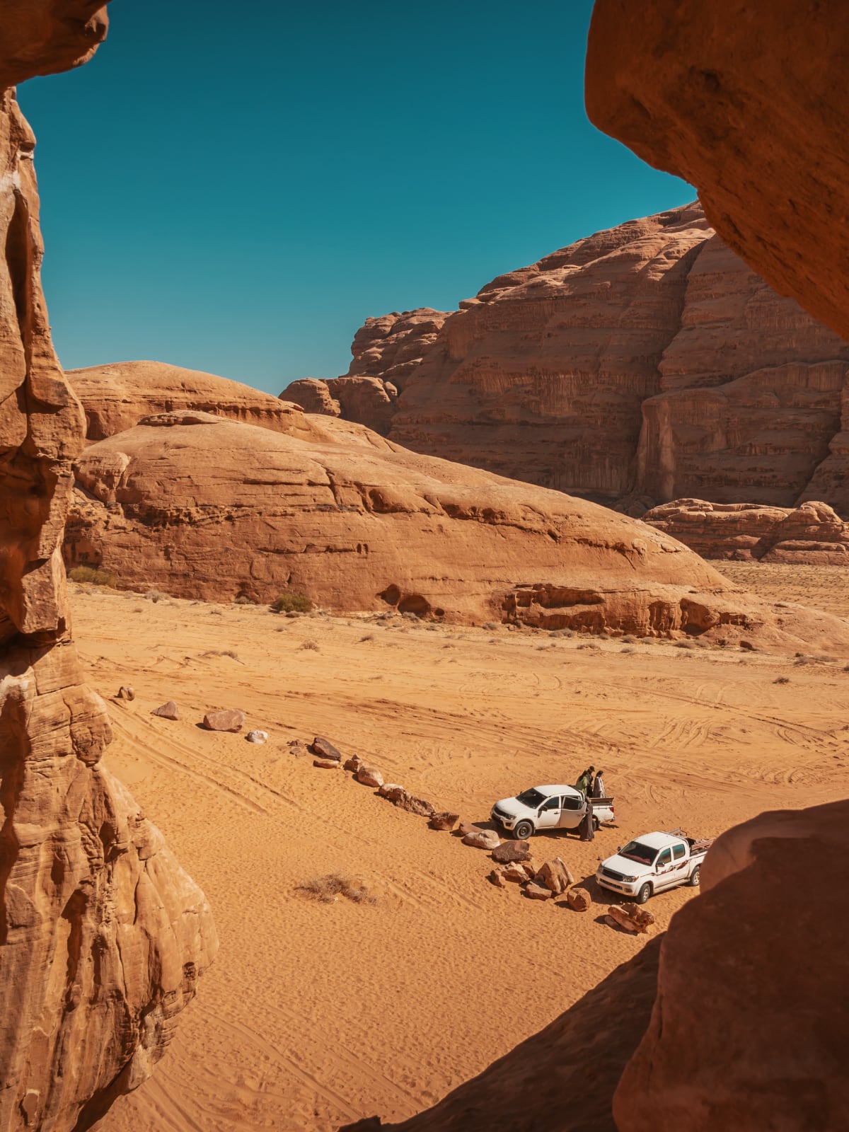 4x4 trucks parked among red rock formations in the Wadi Rum desert, Jordan.