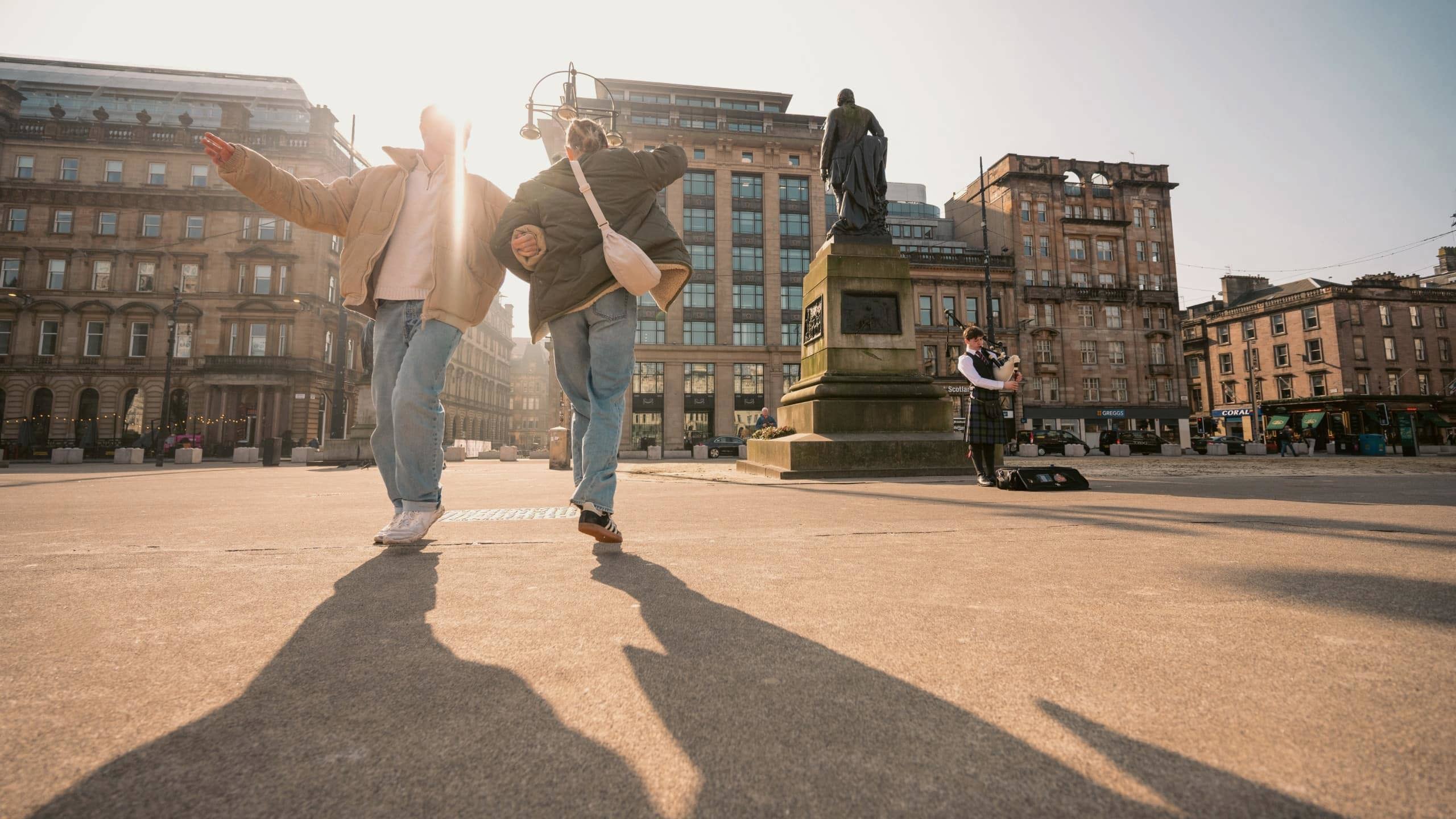 Travellers explore George Square in Glasgow while a bagpiper performs on the Contiki Best of England & Scotland Tour
