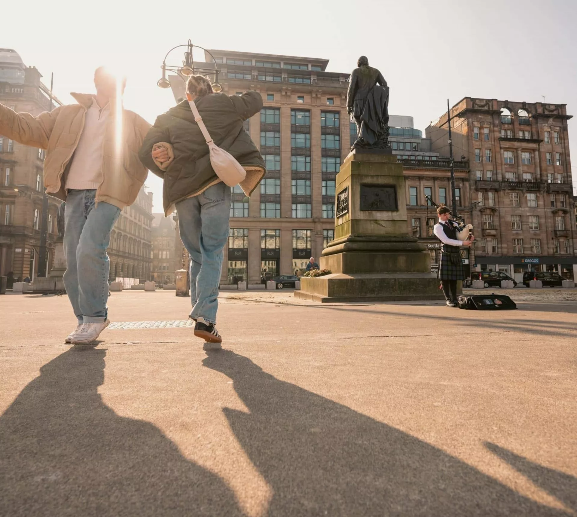 Travellers explore George Square in Glasgow while a bagpiper performs on the Contiki Best of England & Scotland Tour