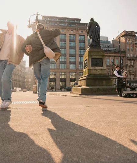 Travellers explore George Square in Glasgow while a bagpiper performs on the Contiki Best of England & Scotland Tour