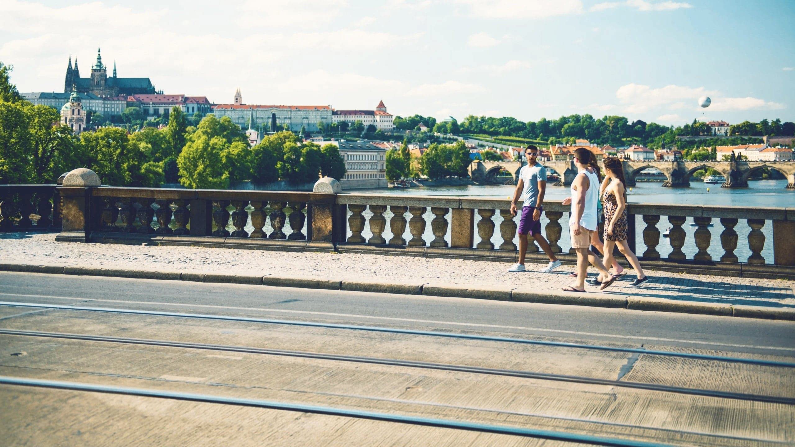 Contiki travellers walk across Prague's Charles Bridge with Prague Castle and the Vltava River in the background on the London to Rome Trail Tour