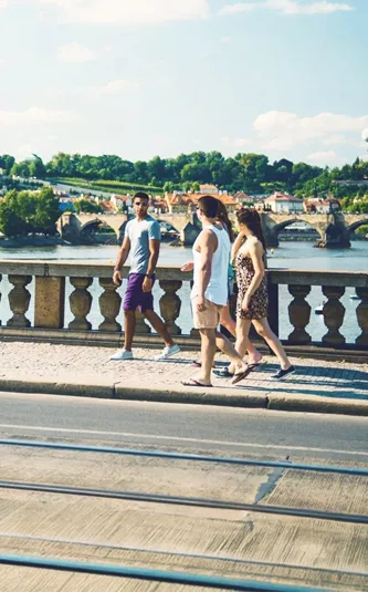 Contiki travellers walk across Prague's Charles Bridge with Prague Castle and the Vltava River in the background on the London to Rome Trail Tour