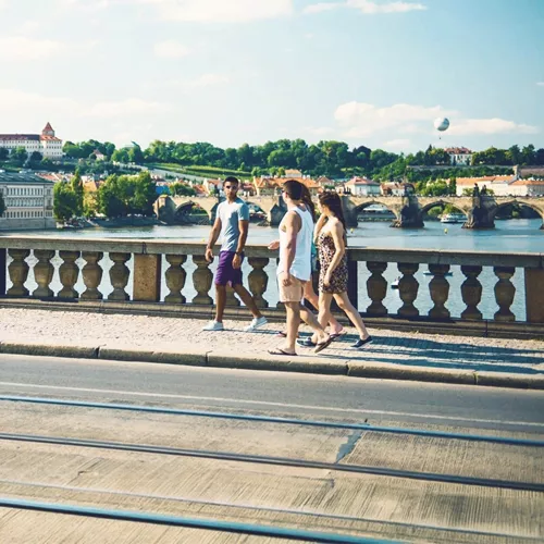 Contiki travellers walk across Prague's Charles Bridge with Prague Castle and the Vltava River in the background on the London to Rome Trail Tour