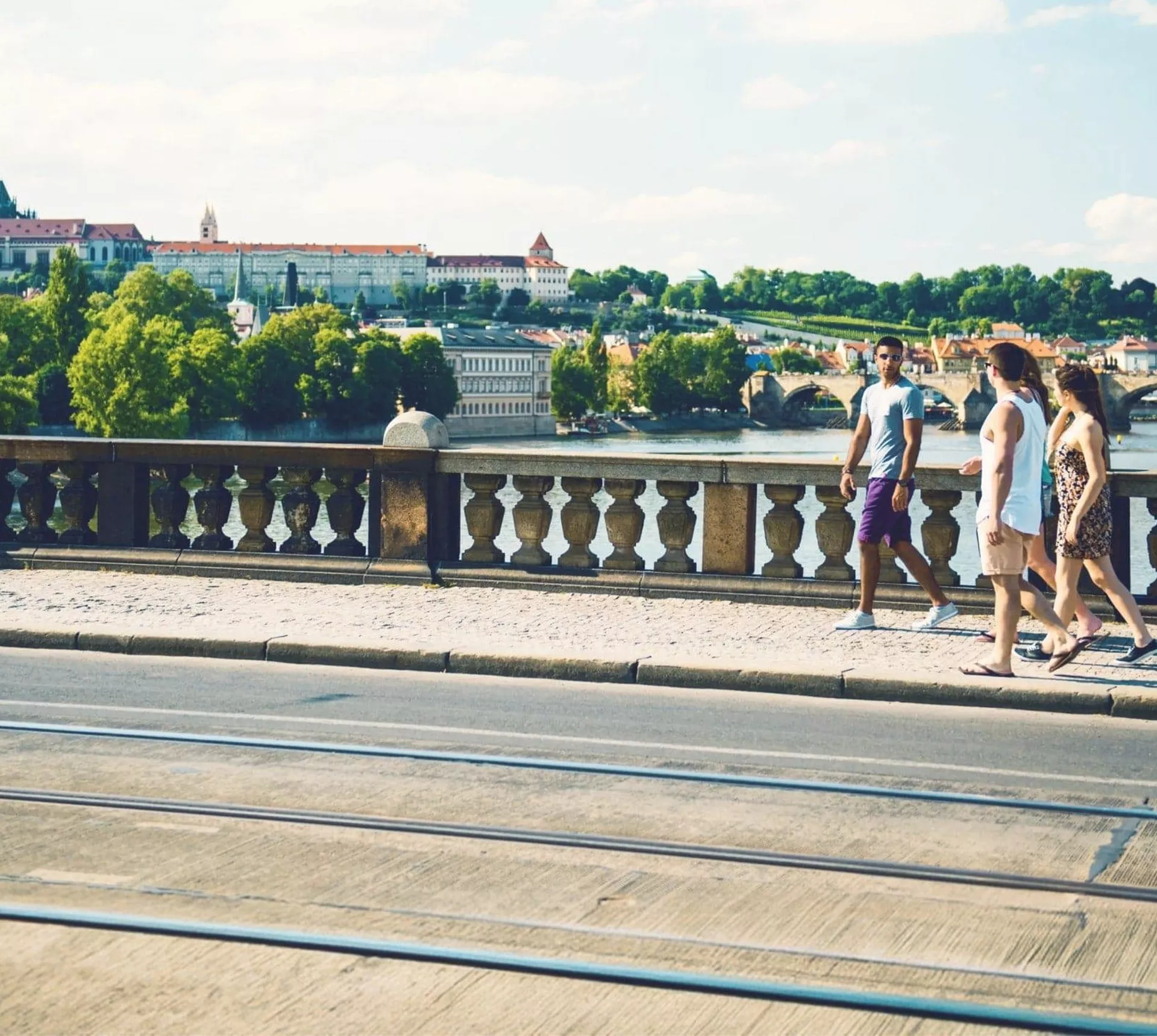 Contiki travellers walk across Prague's Charles Bridge with Prague Castle and the Vltava River in the background on the London to Rome Trail Tour