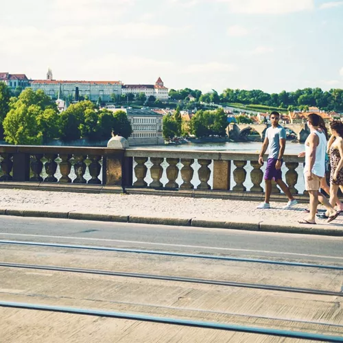 Contiki travellers walk across Prague's Charles Bridge with Prague Castle and the Vltava River in the background on the London to Rome Trail Tour