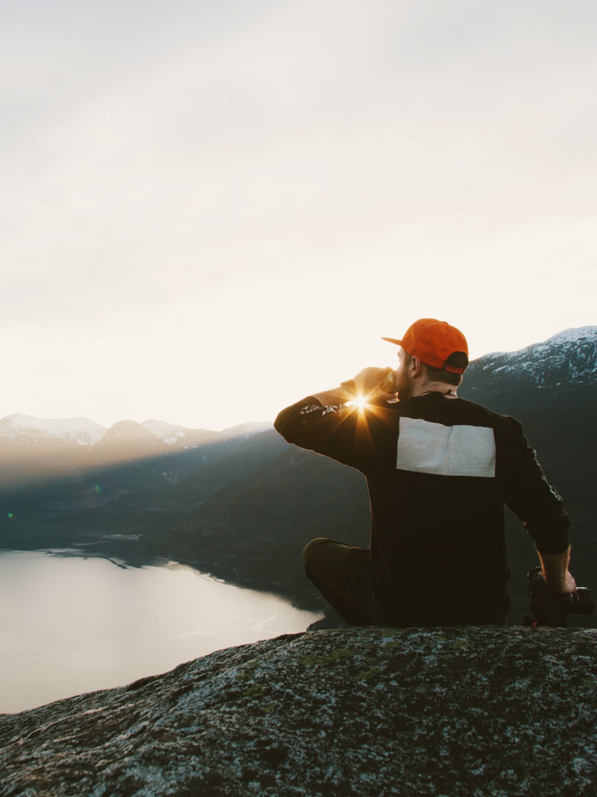 Traveller sitting on a rocky ledge overlooking a fjord and mountains near Vancouver, Canada.