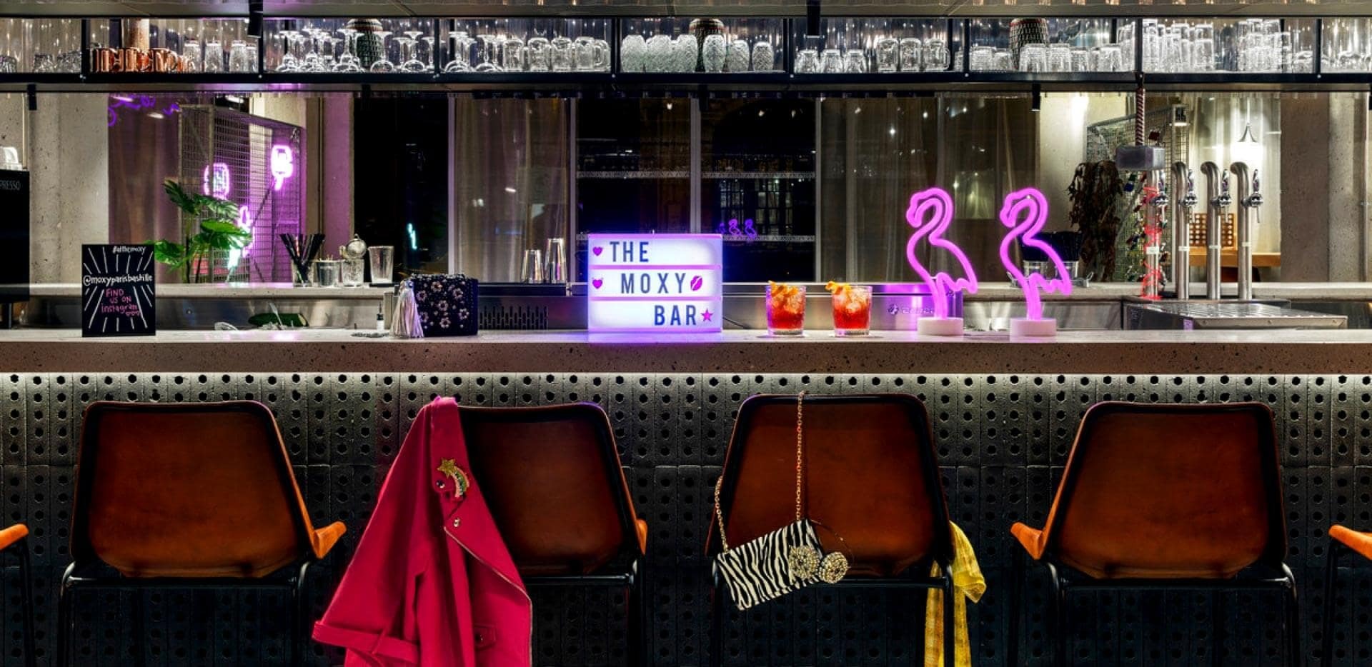  Moxy Paris Bastille cocktail bar with row of red chairs and neon flamingos