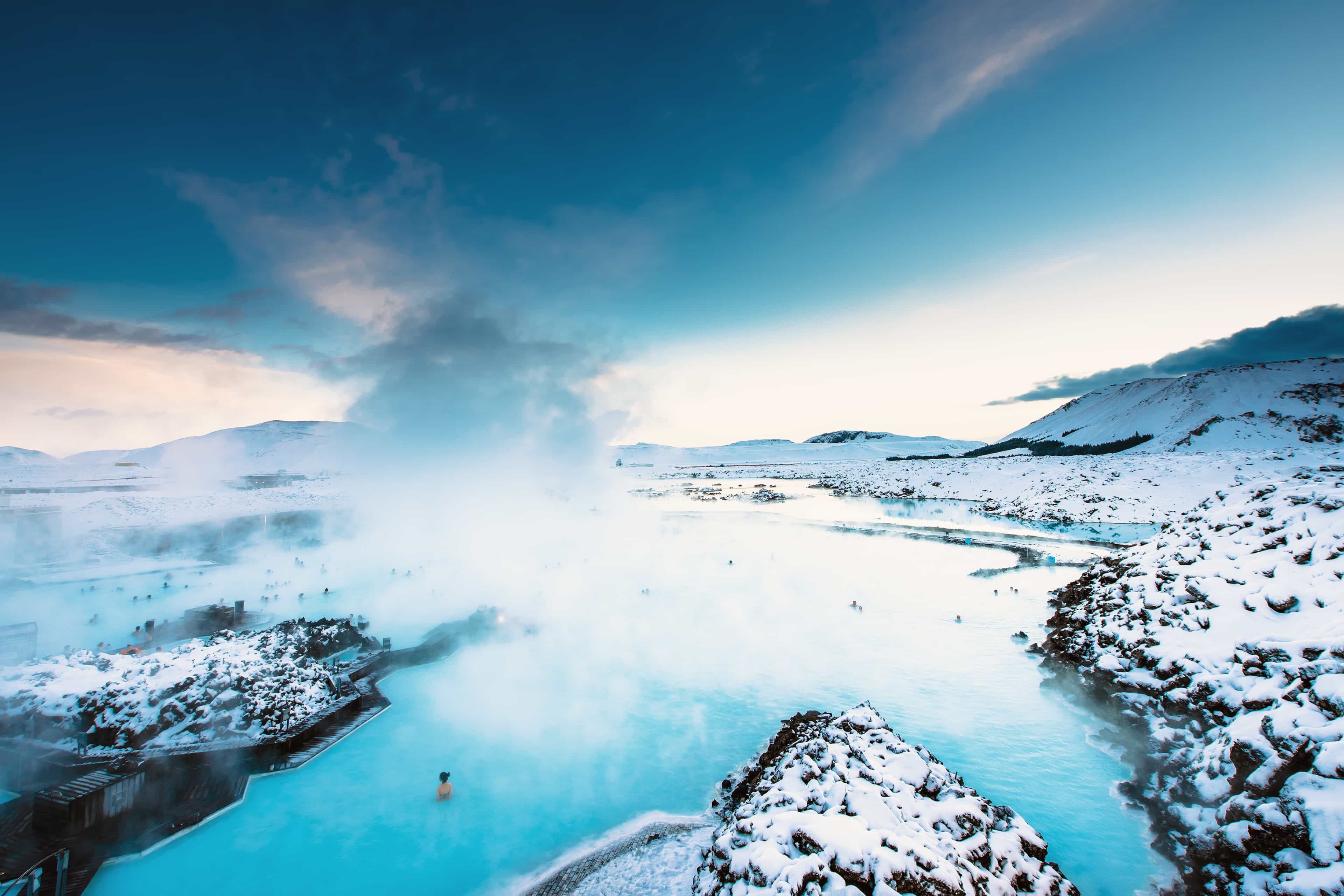 Steam rising off the milky-blue geothermal waters of the Blue Lagoon surrounded by snow-covered lava fields, Iceland.