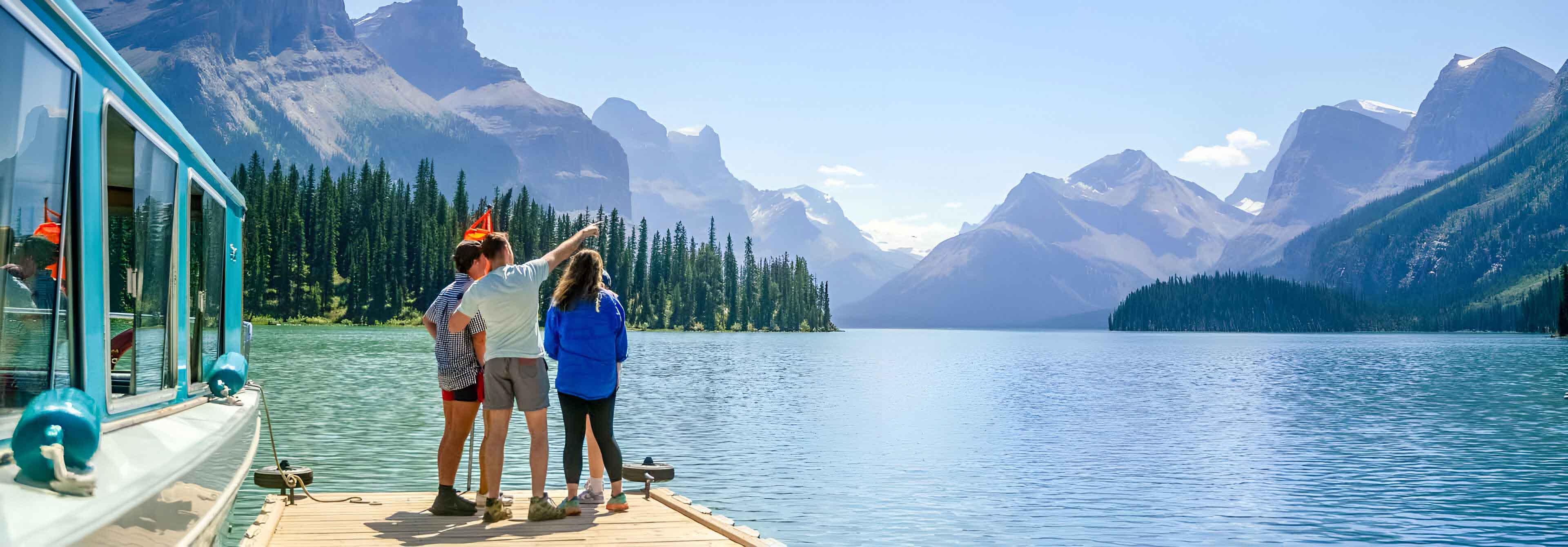 Three People Looking Over Lake and Mountains Man Pointing to Sky