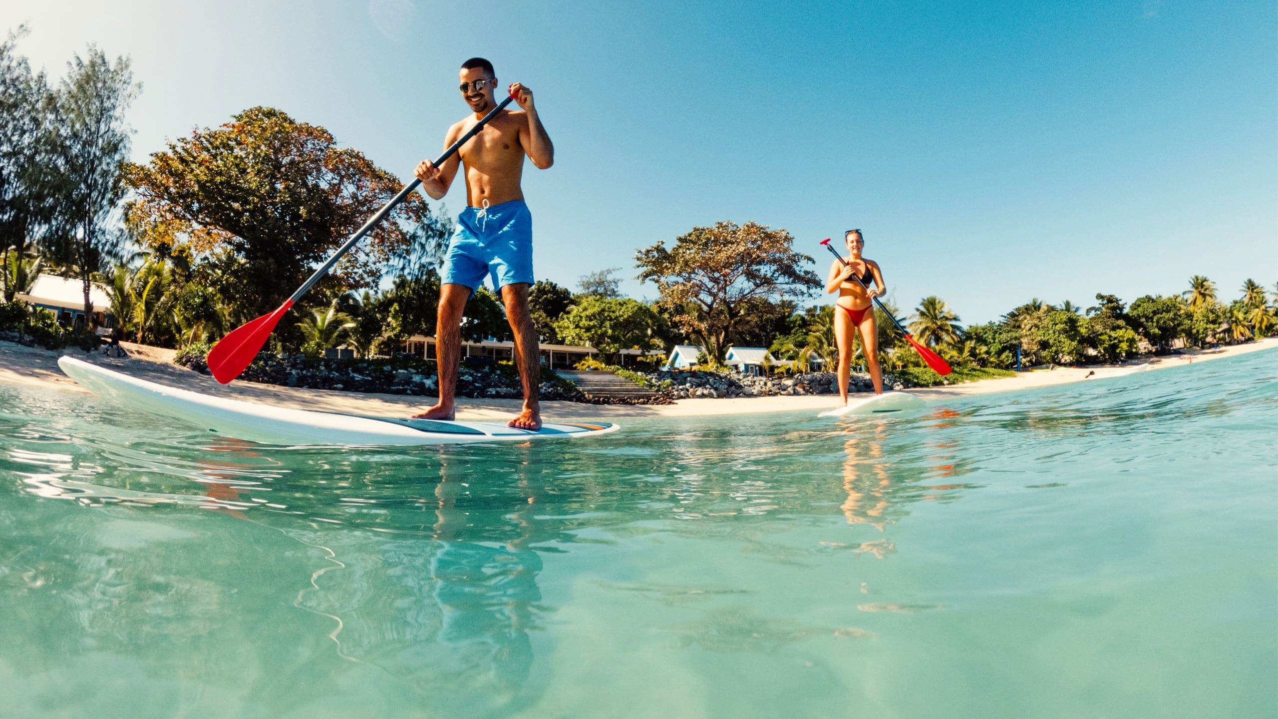 Travellers stand-up paddleboarding in the turquoise waters of Fiji during a Contiki Fiji Island Hopping Adventure