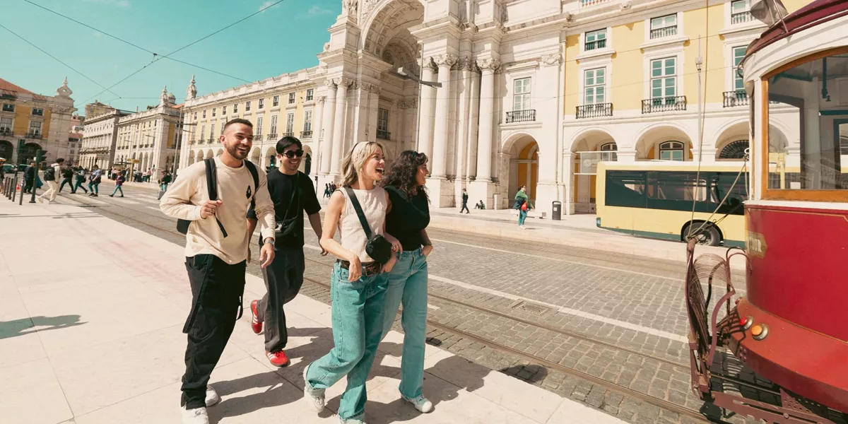 Contiki travellers exploring Lisbon’s Praça do Comércio beside the iconic yellow tram, discovering historic landmarks on the Spain & Portugal Panorama Tour