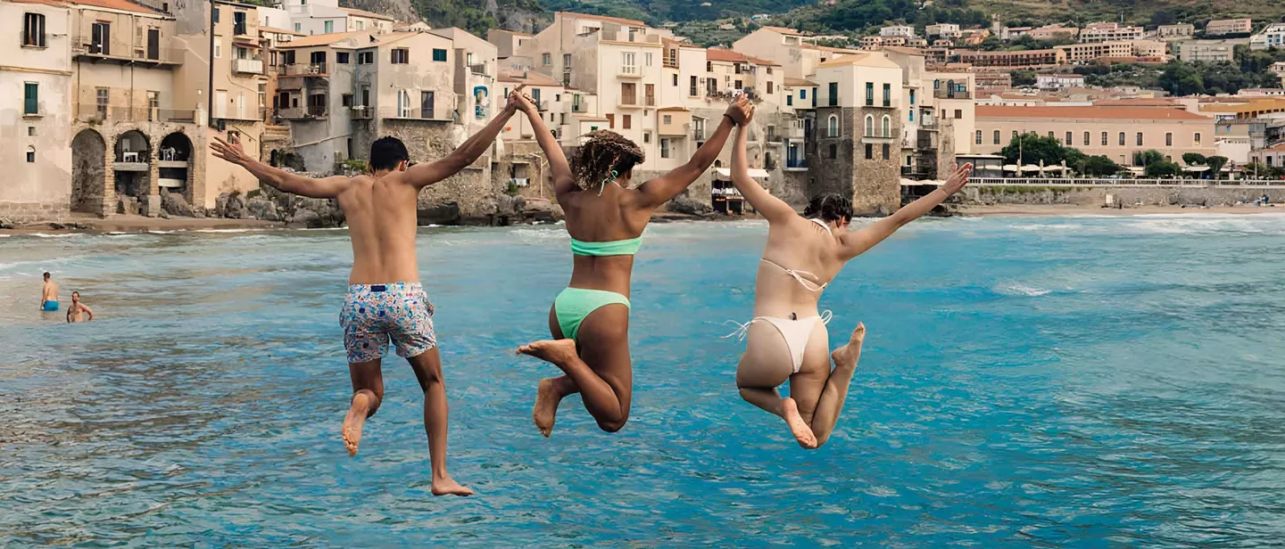 Three Young Travelers Jumping Into Sea In Sicily