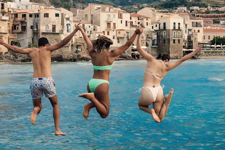 Three Young Travelers Jumping Into Sea In Sicily