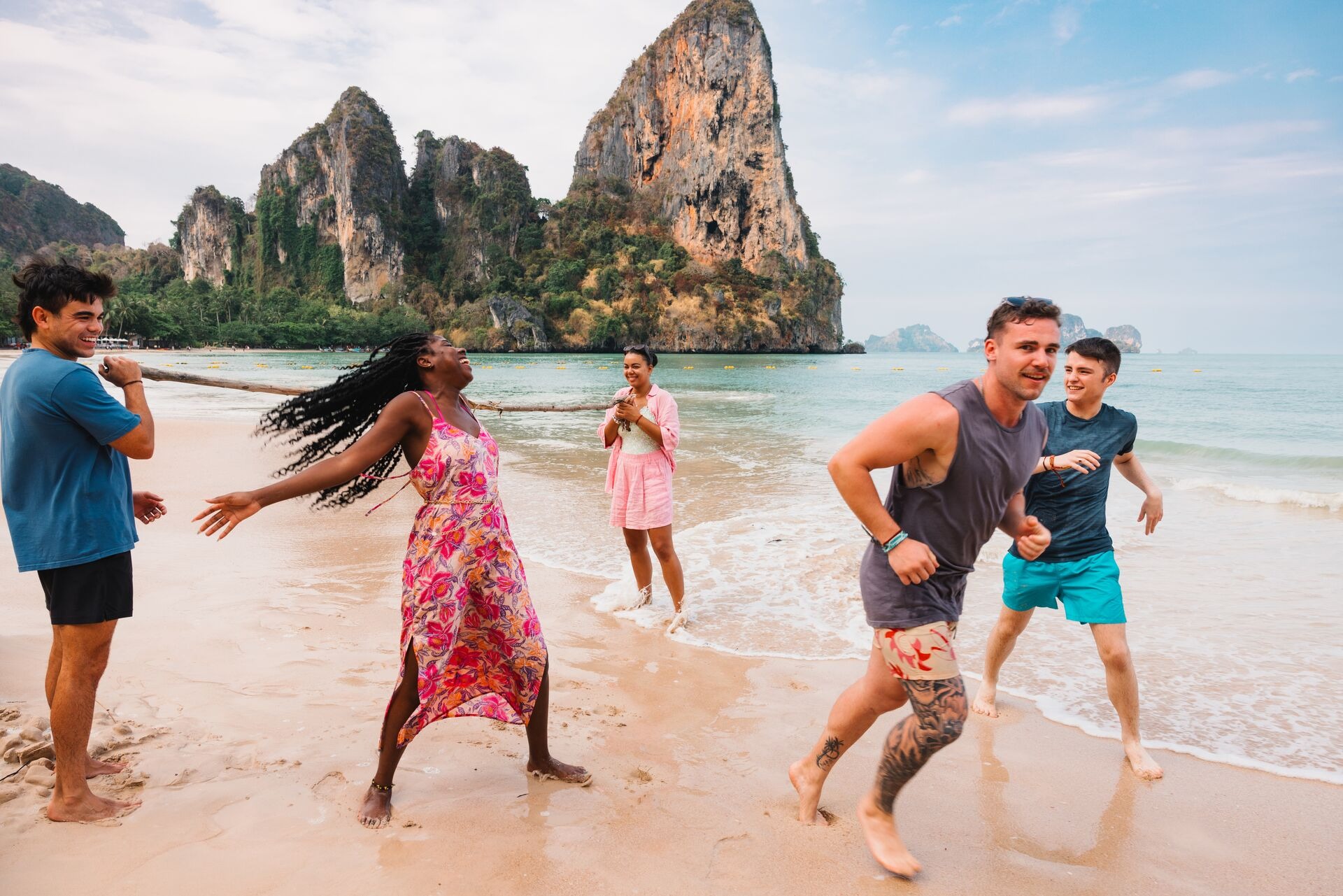A group of friends laughing and enjoying their time together on a sunny beach, surrounded by sand and waves.