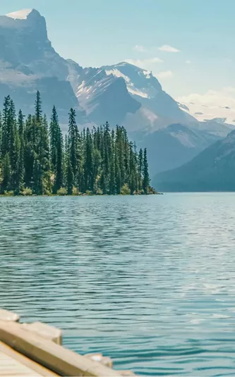 Three travellers sitting on a wooden dock at Maligne Lake in Jasper National Park overlooking Spirit Island and the dramatic Canadian Rocky Mountain peaks in Alberta - Contiki Canada Vancouver and the Rockies Tour