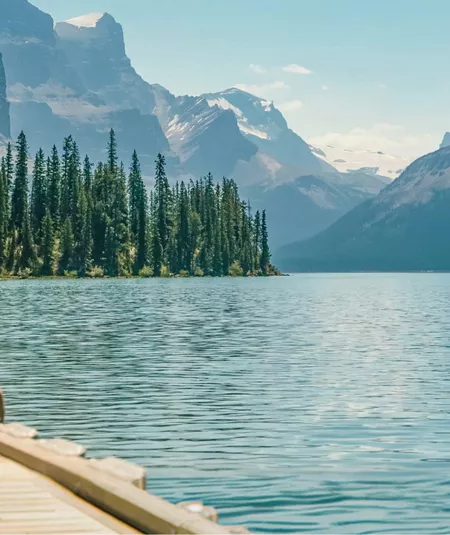 Three travellers sitting on a wooden dock at Maligne Lake in Jasper National Park overlooking Spirit Island and the dramatic Canadian Rocky Mountain peaks in Alberta - Contiki Canada Vancouver and the Rockies Tour