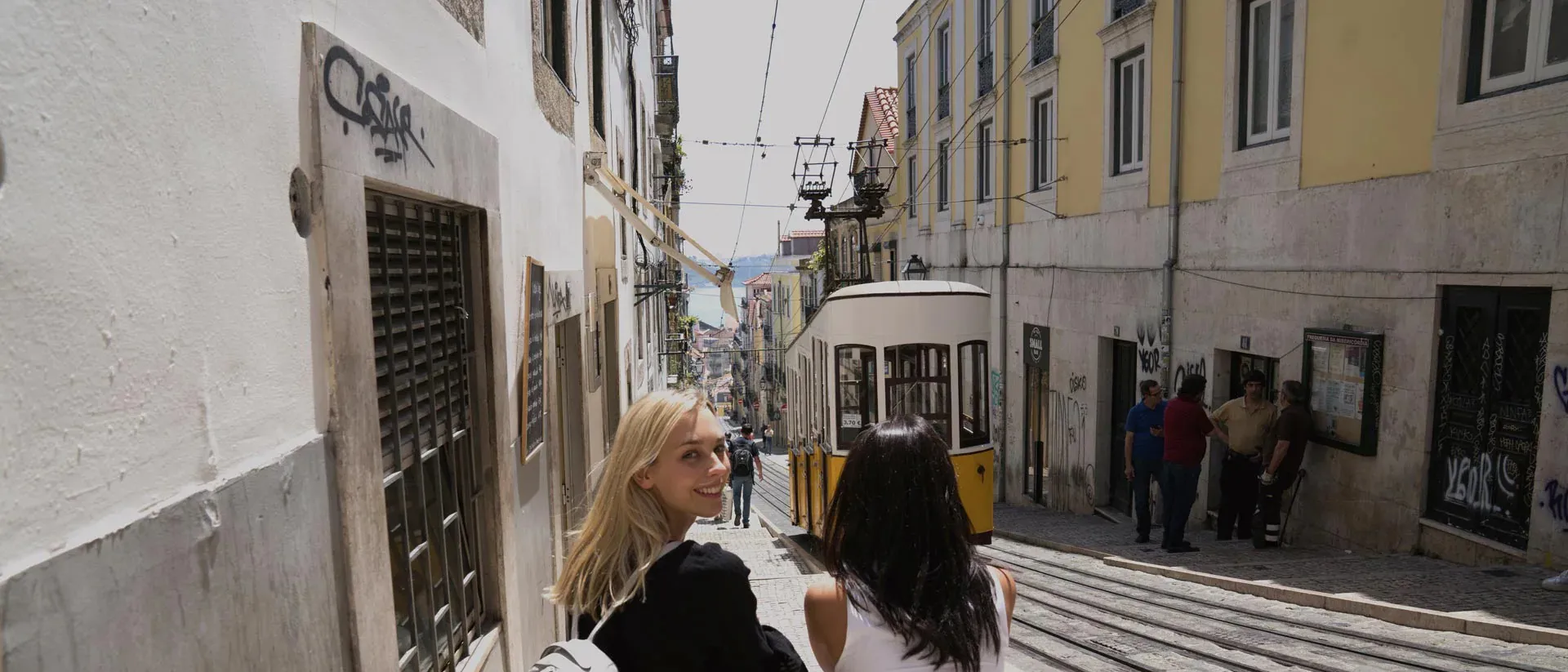 Two tourists walking an old narrow street with streetcar in Lisbon, Portugal