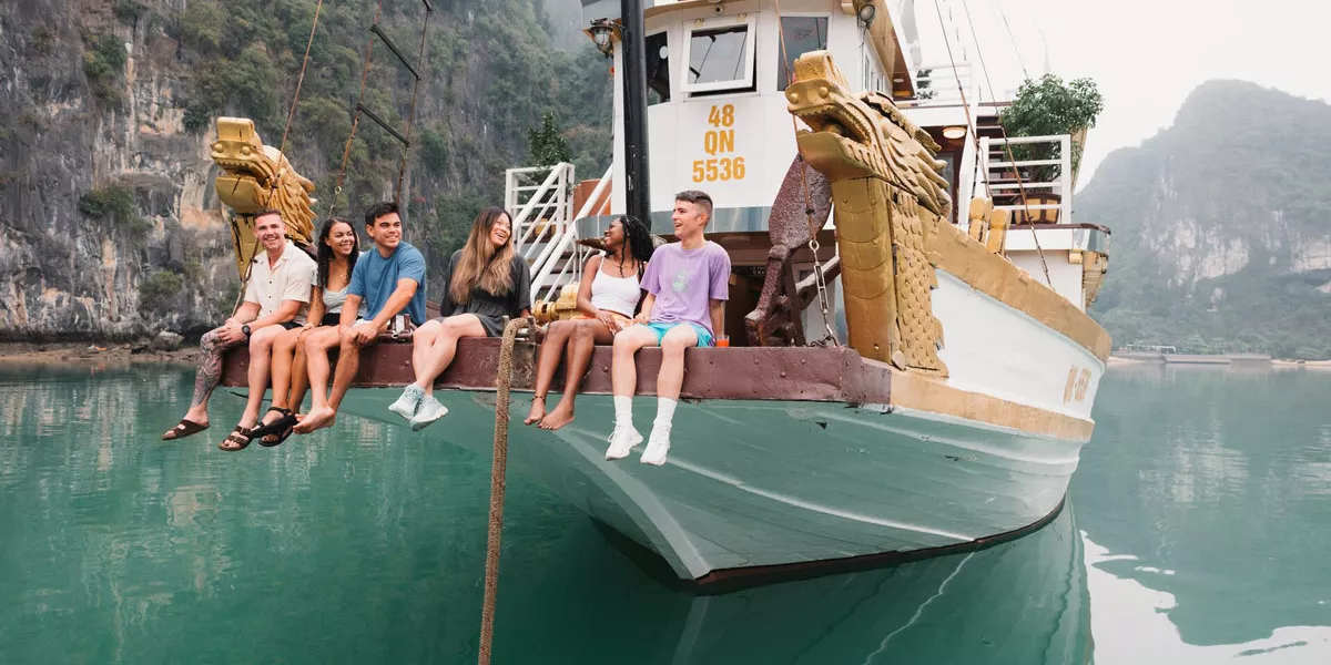 Groupd Of Young People Sitting At The Edge Of A Boat Enjoying The Landscape