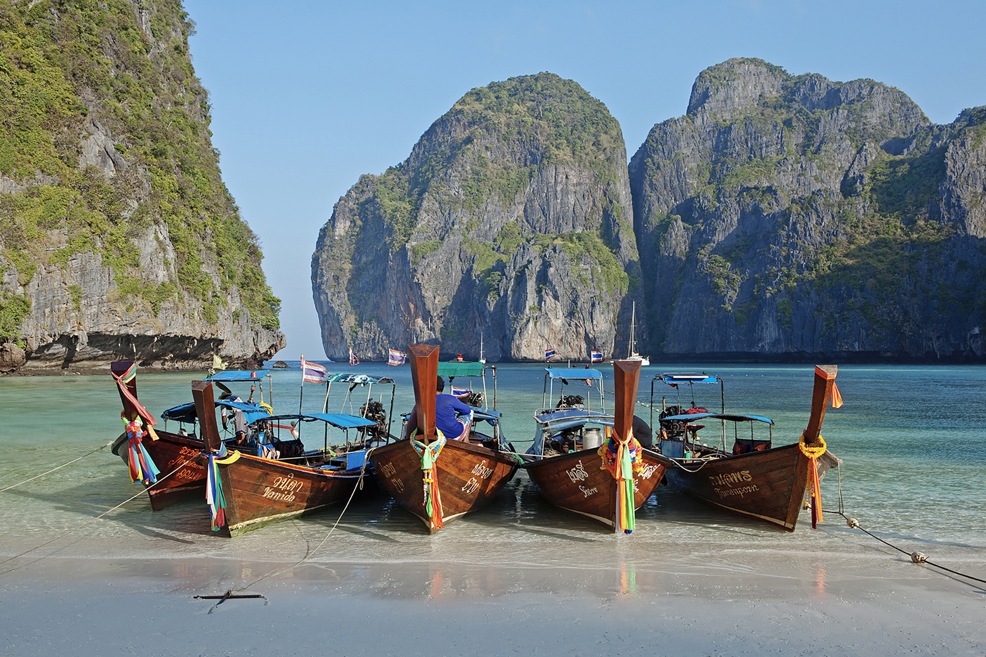 Four boats sitting on the edge of a beach in Thailand