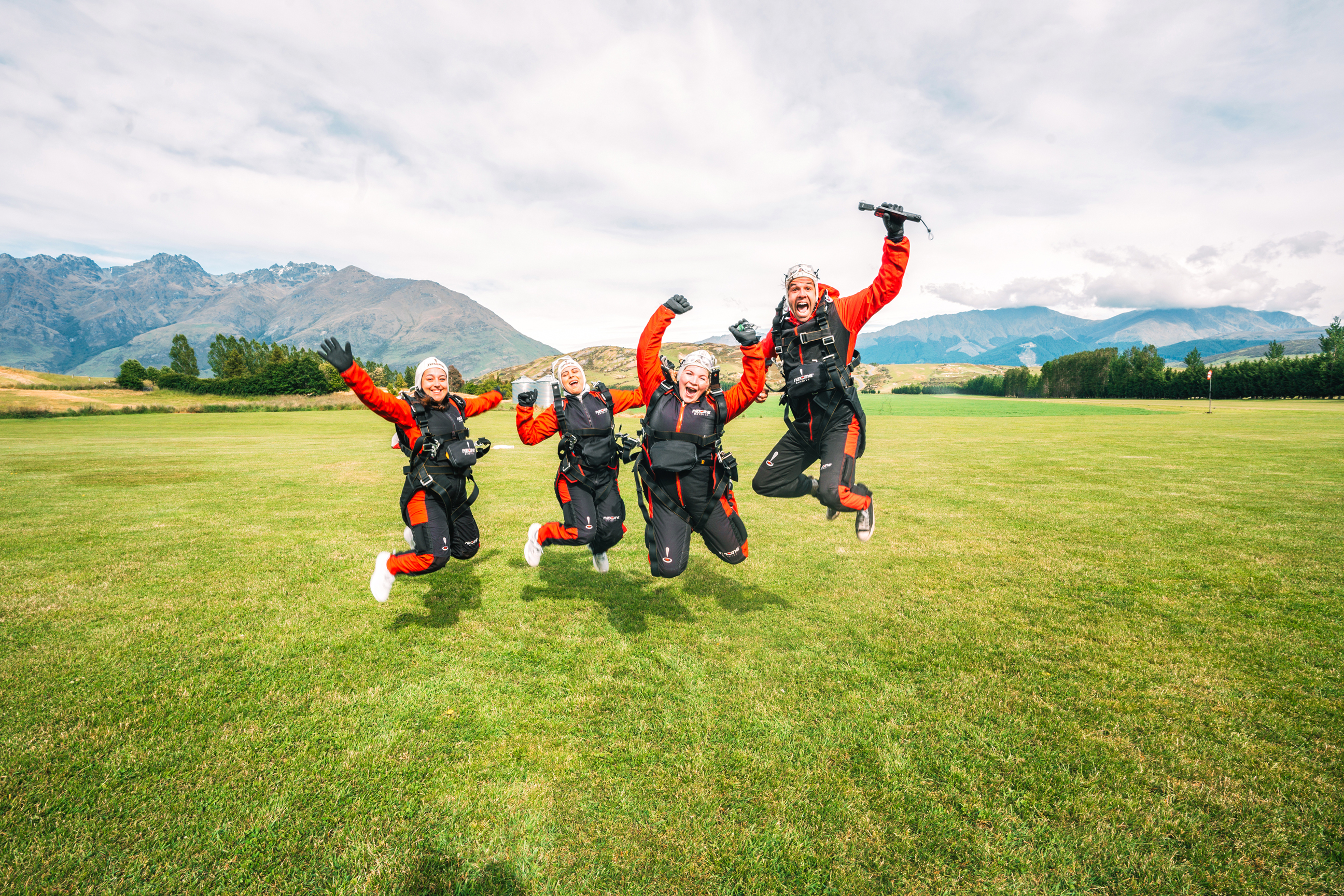 Four travellers wearing skydiving outfits jumping in the air, Franz Josef, New Zealand
