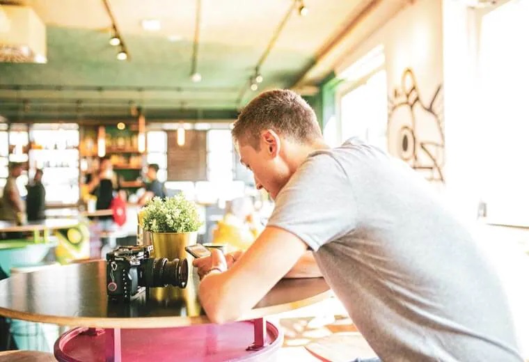 Young man sitting by the table with camera, checking mobile