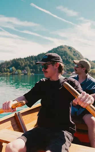 Travellers take in stunning mountain views while rowing across an emerald lake on the Contiki Budapest to Dubrovnik Tour