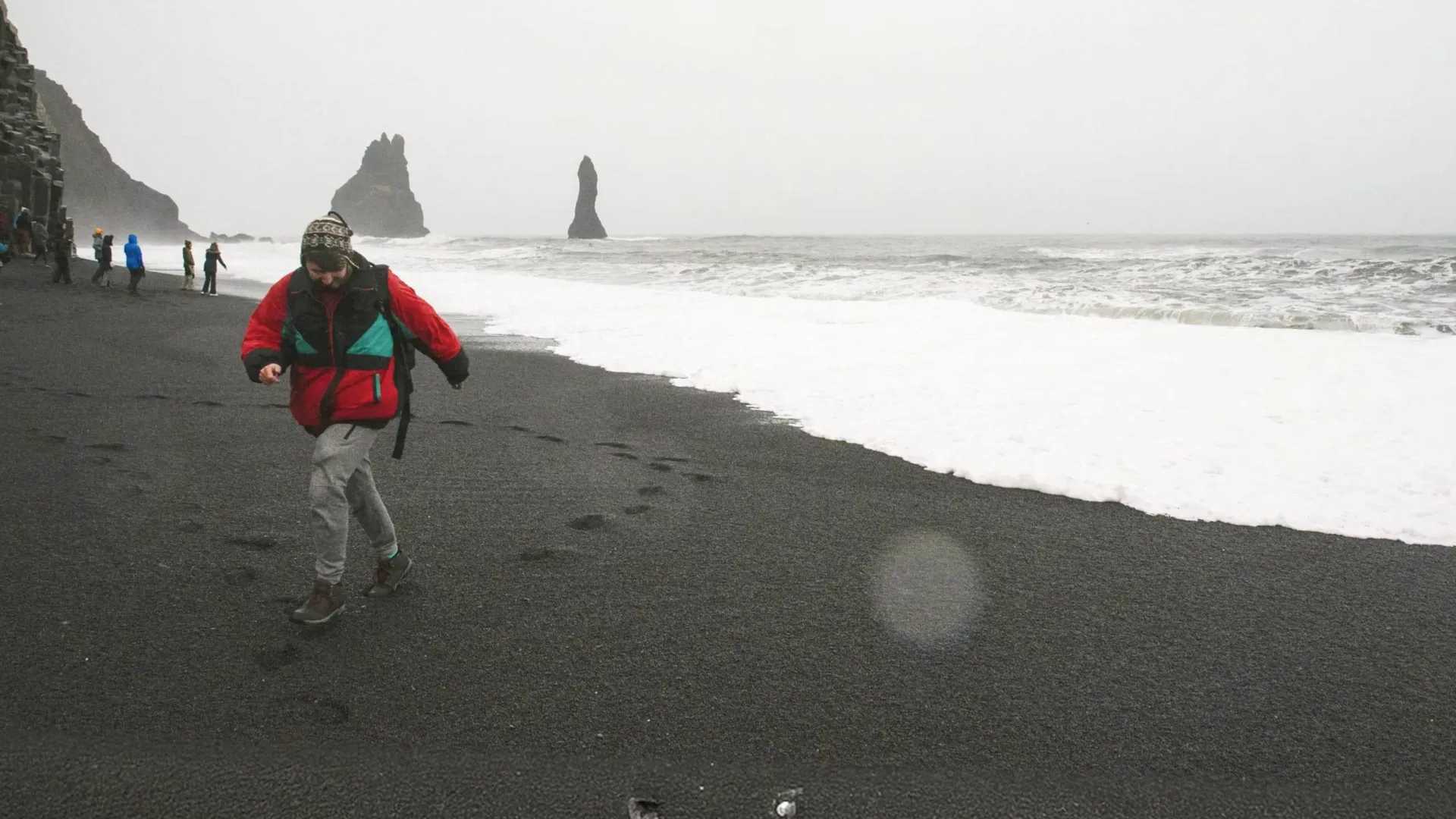 Traveller walks along Reynisfjara Black Sand Beach with the Reynisdrangar sea stacks in Iceland on the Contiki Best of Iceland Tour