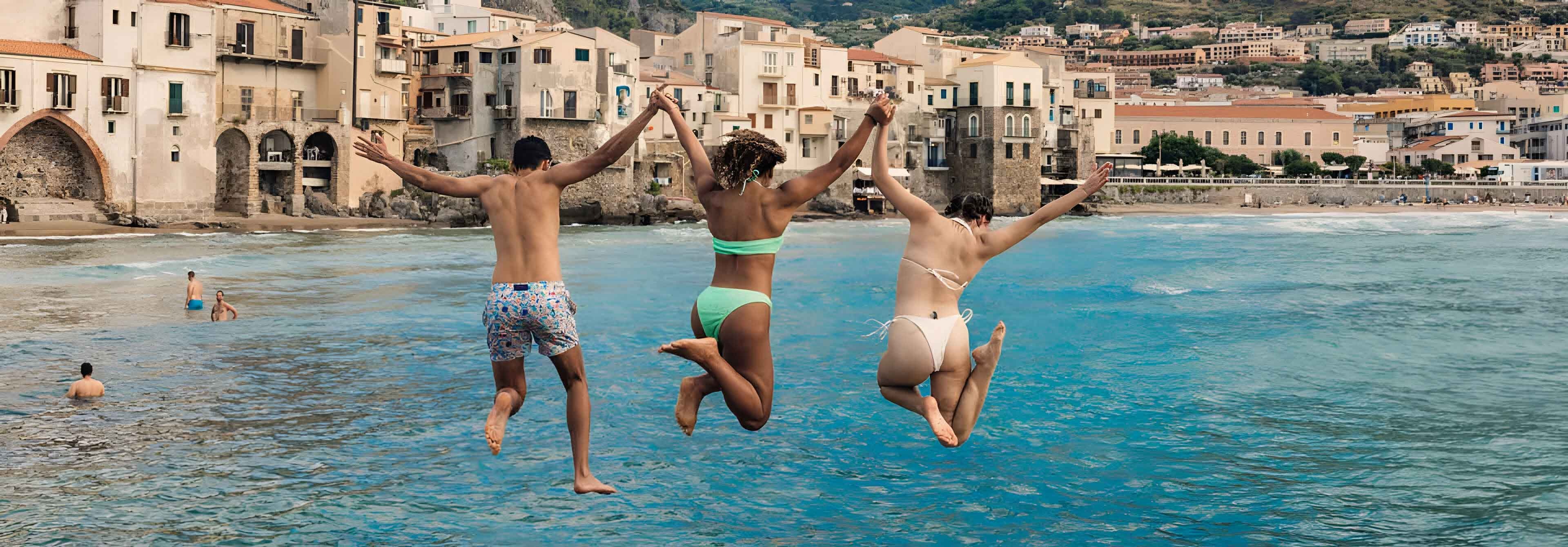 Three Young Travelers Jumping Into Sea In Sicily