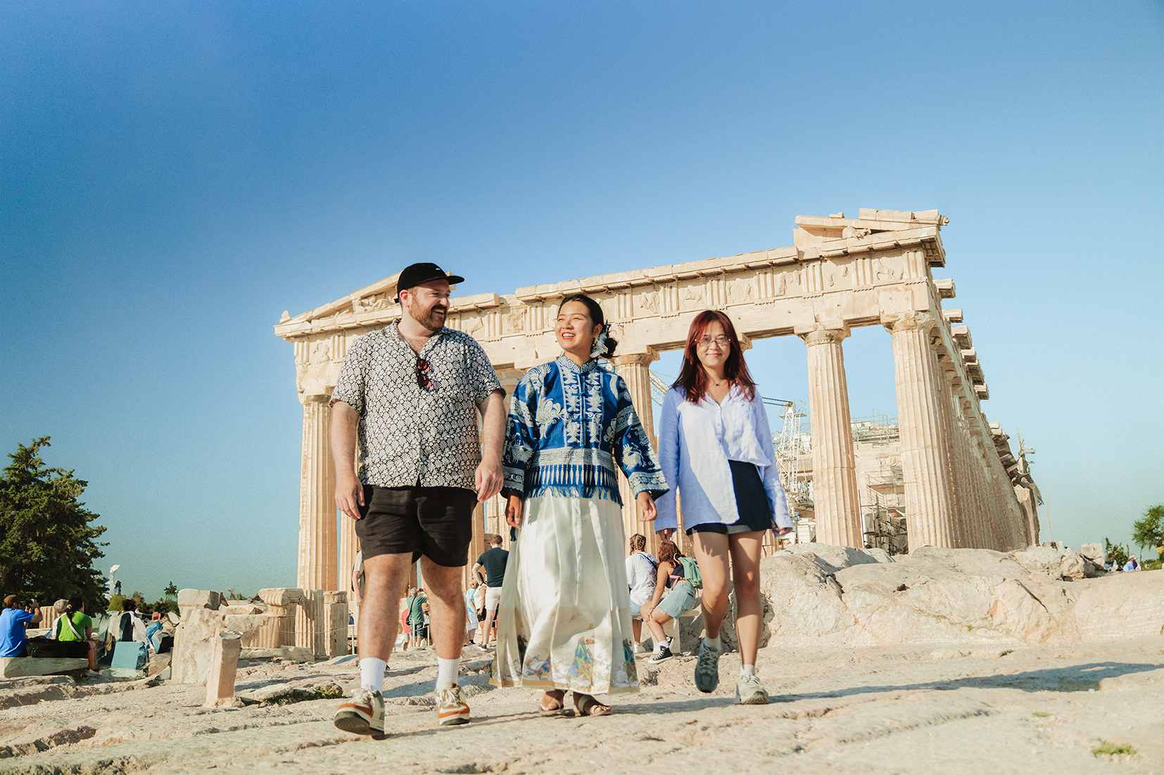 Three travellers smiling walking towards the camera in the sun on the Acropolis in Athens, Greece