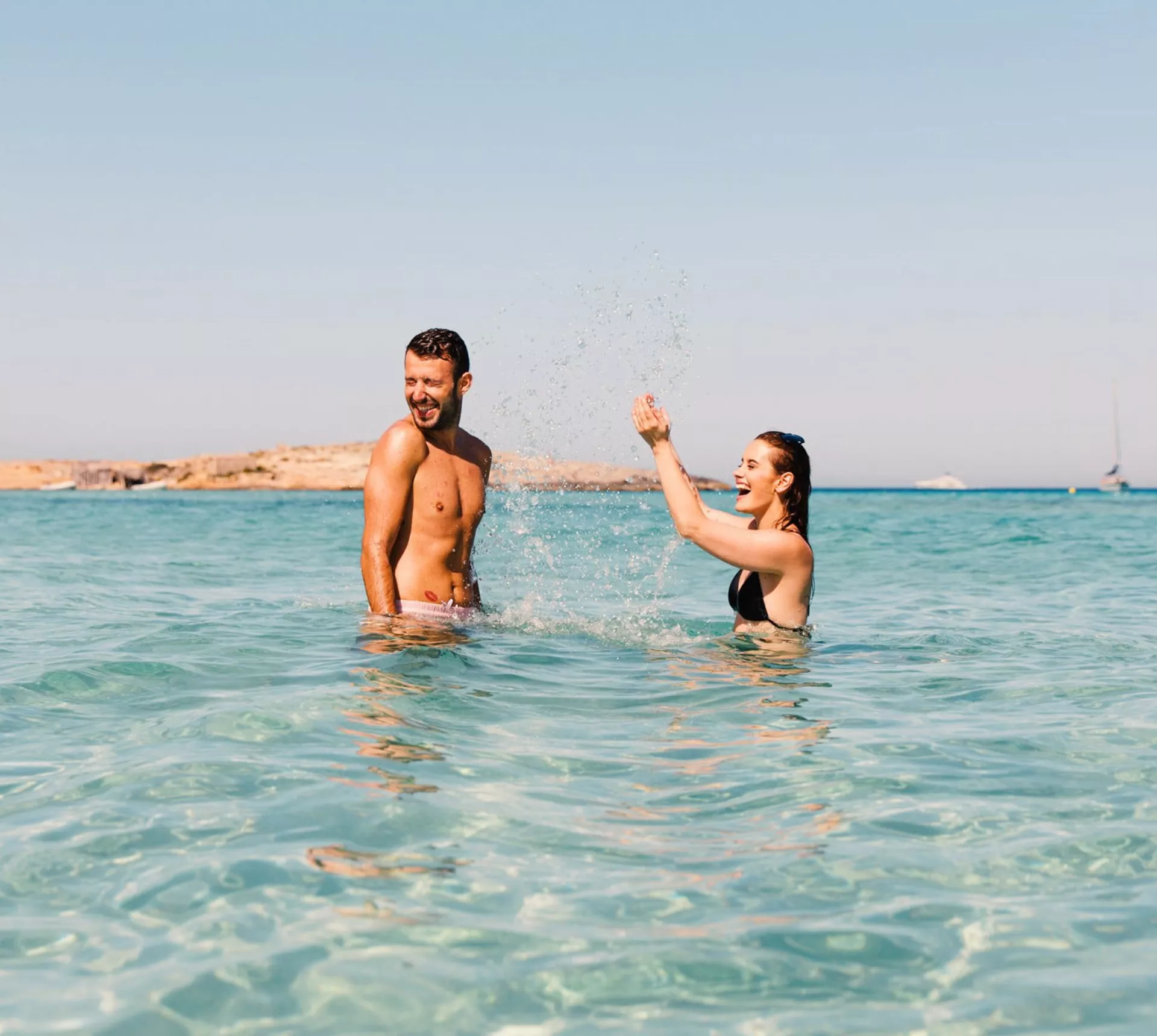 Two young travellers laughing and splashing in crystal clear turquoise waters off the Spanish coast - Contiki Ibiza & Mallorca Island Hopping Tour