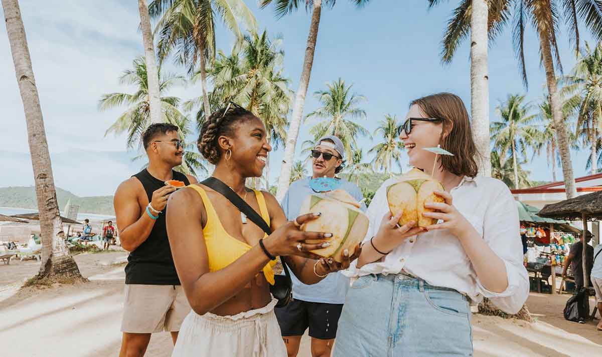 Friends talking and drinking coconut near the beach in the Philippines. 