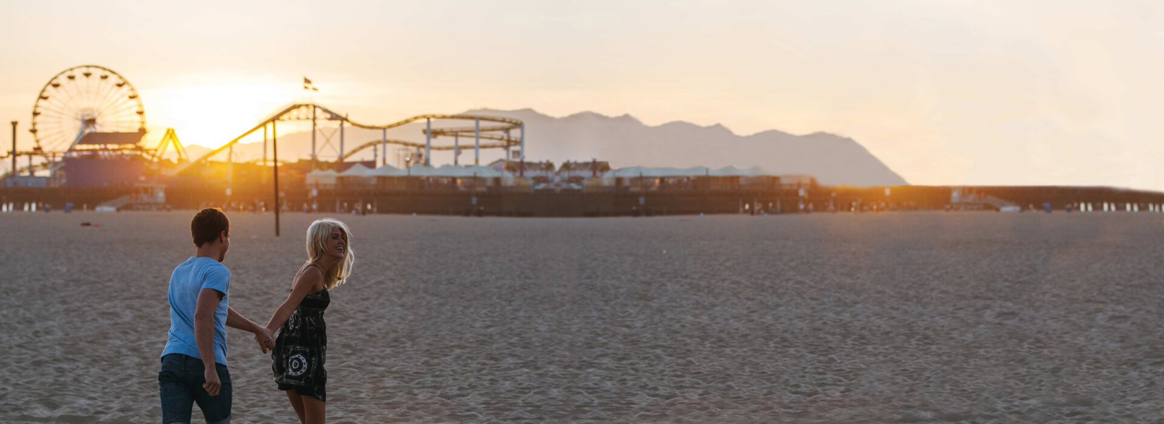 Couple holding hands on Santa Monica Beach at sunset, California, USA