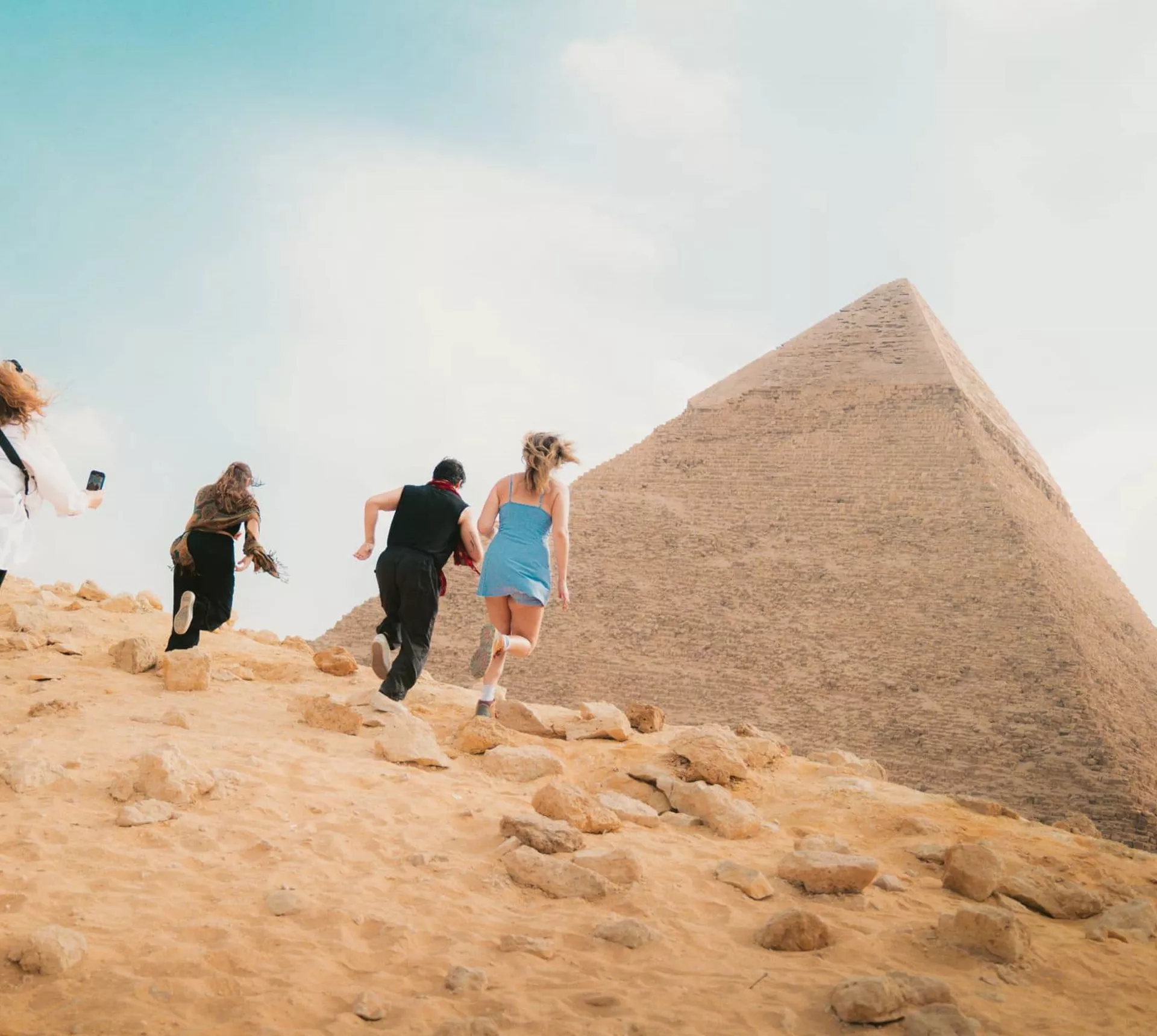 Young travellers running beside the Great Pyramid of Giza in the Egyptian desert near Cairo - Contiki Egypt Tour