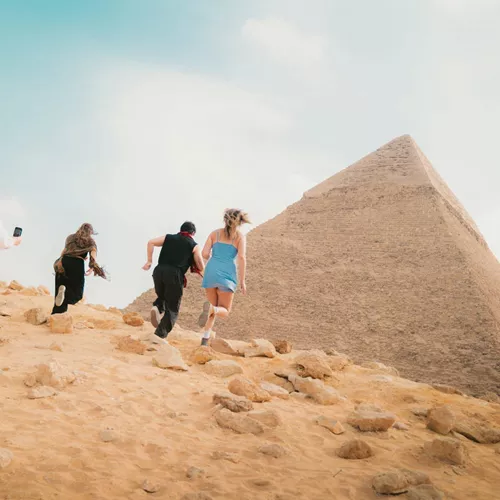 Young travellers running beside the Great Pyramid of Giza in the Egyptian desert near Cairo - Contiki Egypt Tour