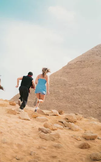 Young travellers running beside the Great Pyramid of Giza in the Egyptian desert near Cairo - Contiki Egypt Tour