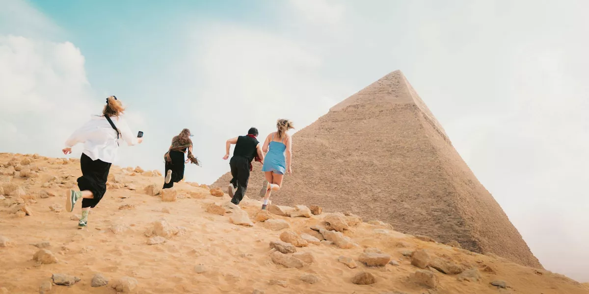 Young travellers running beside the Great Pyramid of Giza in the Egyptian desert near Cairo - Contiki Egypt Tour