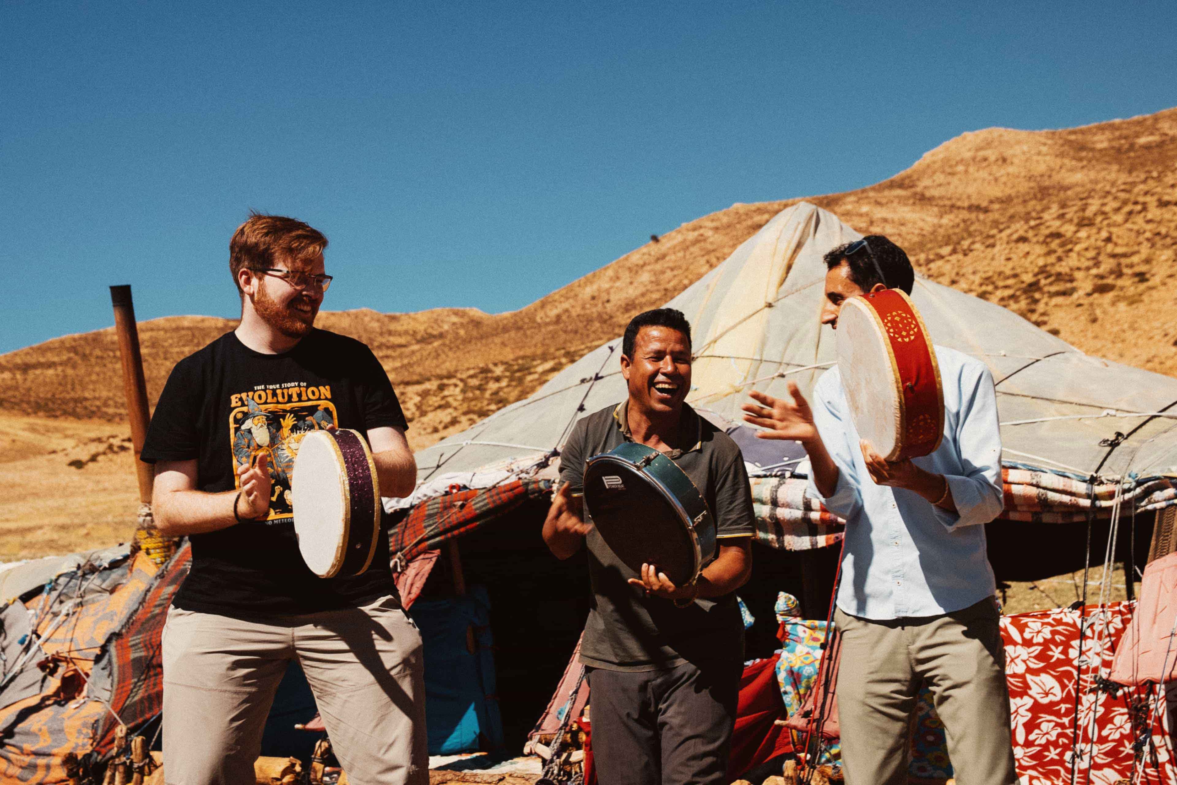A traveller joins local musicians playing hand drums outside a Berber tent camp in Morocco's desert mountains.