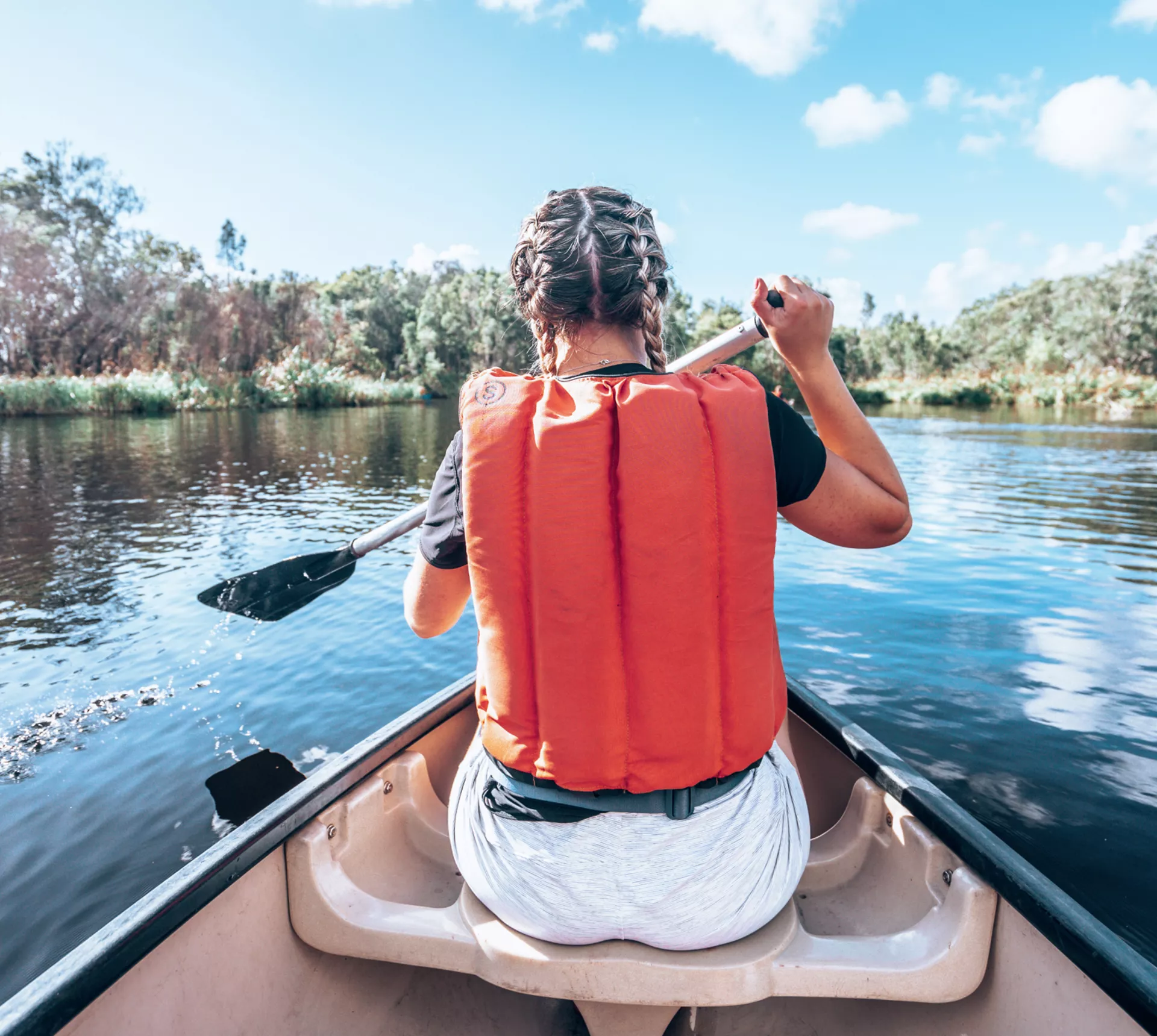 A Contiki travellers paddles a canoe across calm waters, surrounded by native bushland and mirrored reflections in the peaceful wetlands - Sydney to Noosa Tour