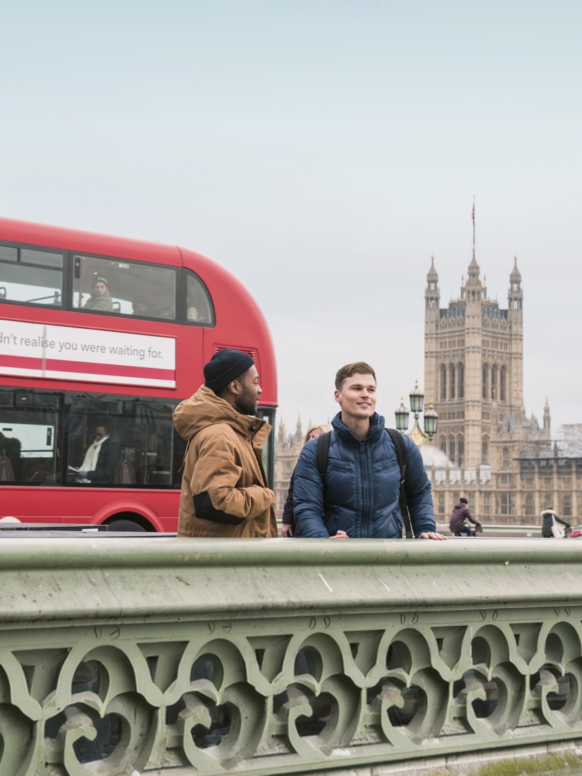 Friends sightseeing near Big Ben and a classic red double-decker bus in London, England.