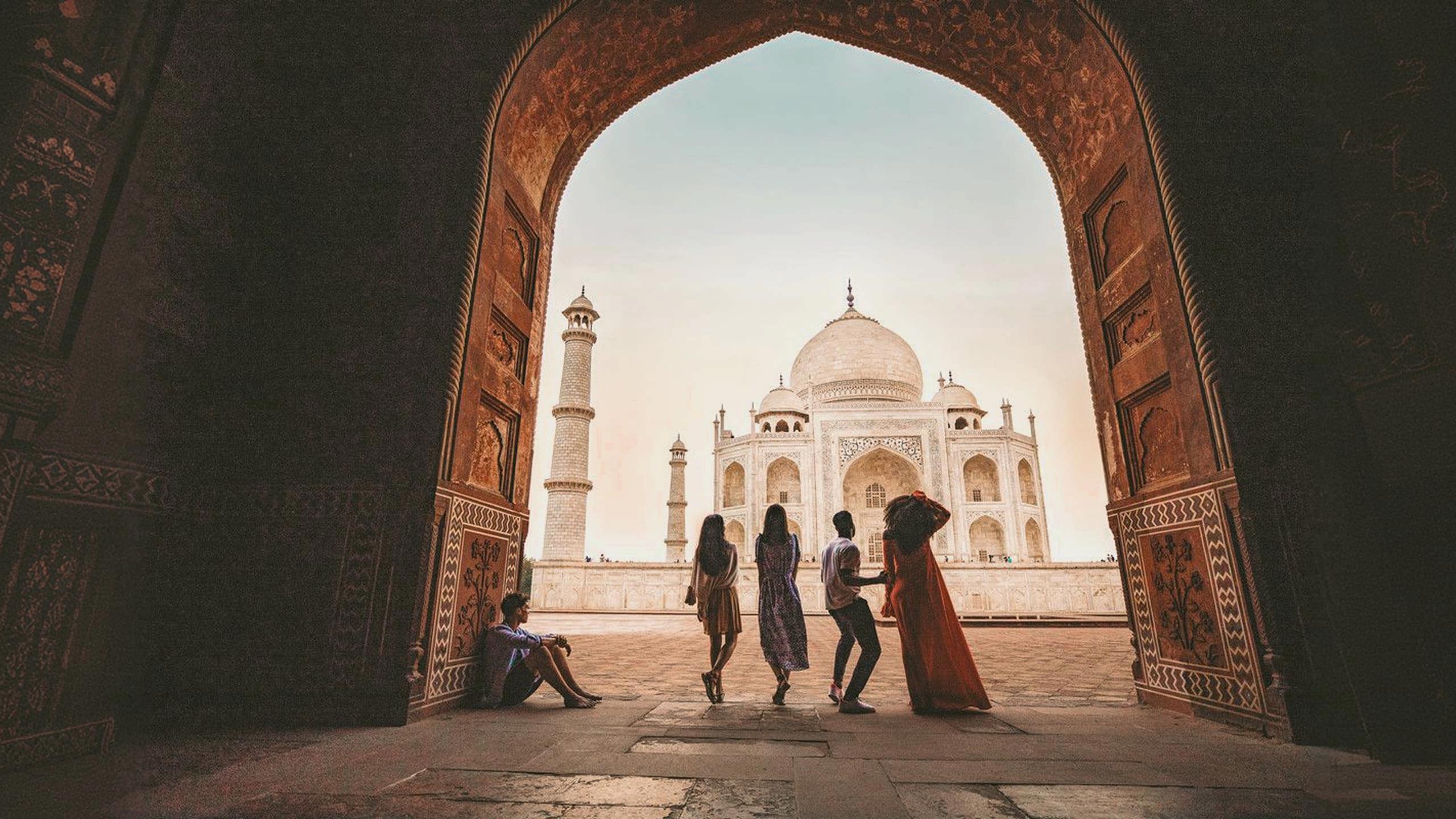Travellers framed through the ornate Great Gate archway looking towards the Taj Mahal white marble mausoleum in Agra India - Contiki Eternal India Tour