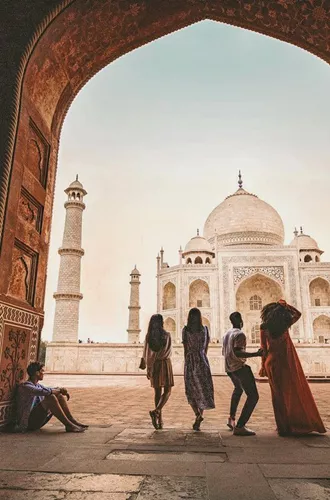Travellers framed through the ornate Great Gate archway looking towards the Taj Mahal white marble mausoleum in Agra India - Contiki Eternal India Tour