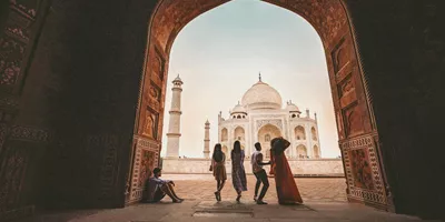 Travellers framed through the ornate Great Gate archway looking towards the Taj Mahal white marble mausoleum in Agra India - Contiki Eternal India Tour