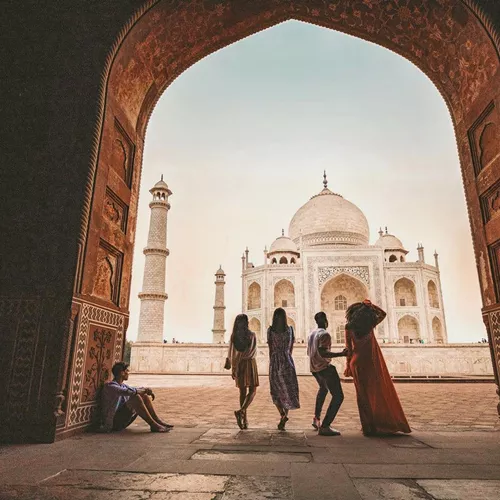 Travellers framed through the ornate Great Gate archway looking towards the Taj Mahal white marble mausoleum in Agra India - Contiki Eternal India Tour