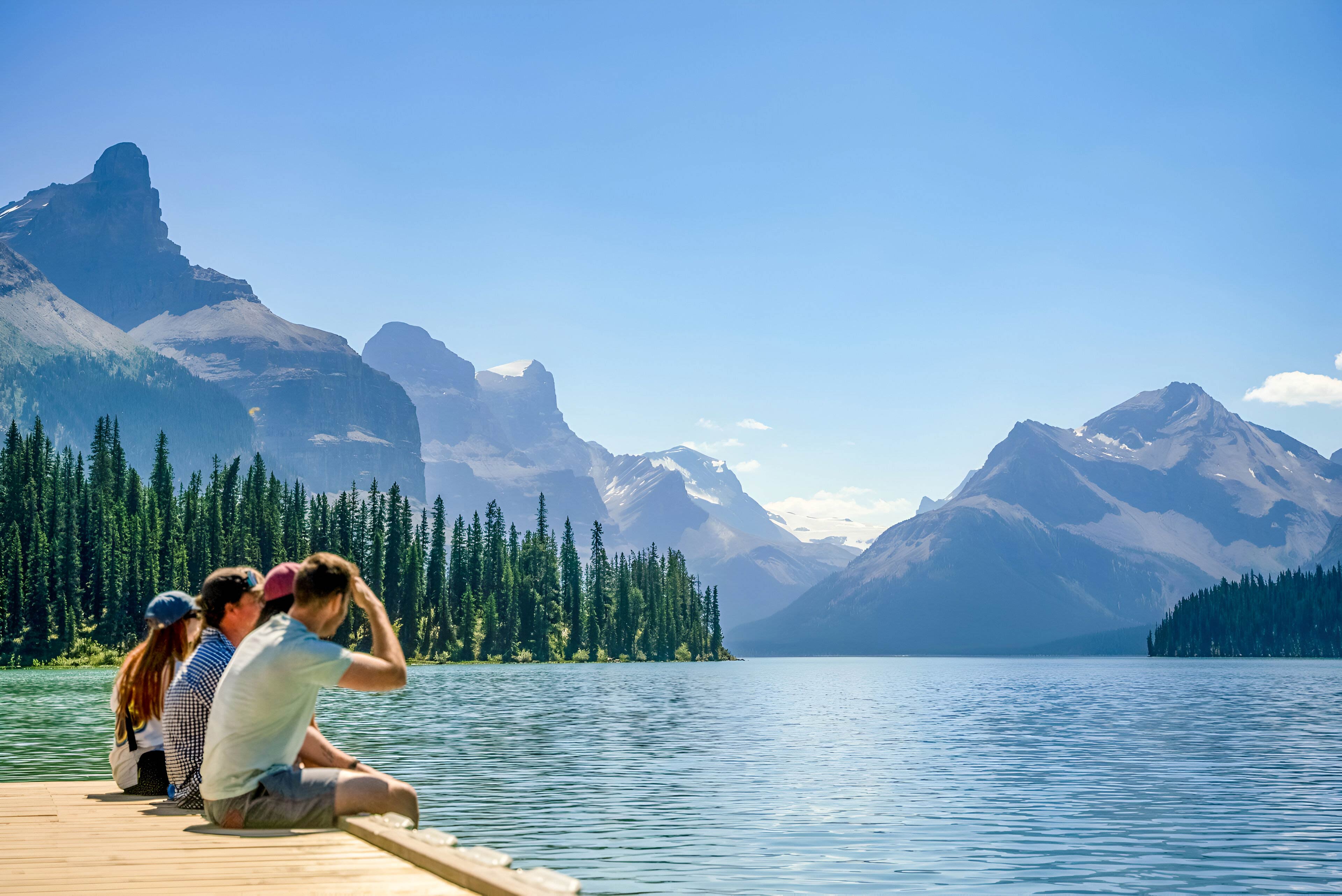 People Sitting Close To A Lake Enjoying The Snowy Mountains View